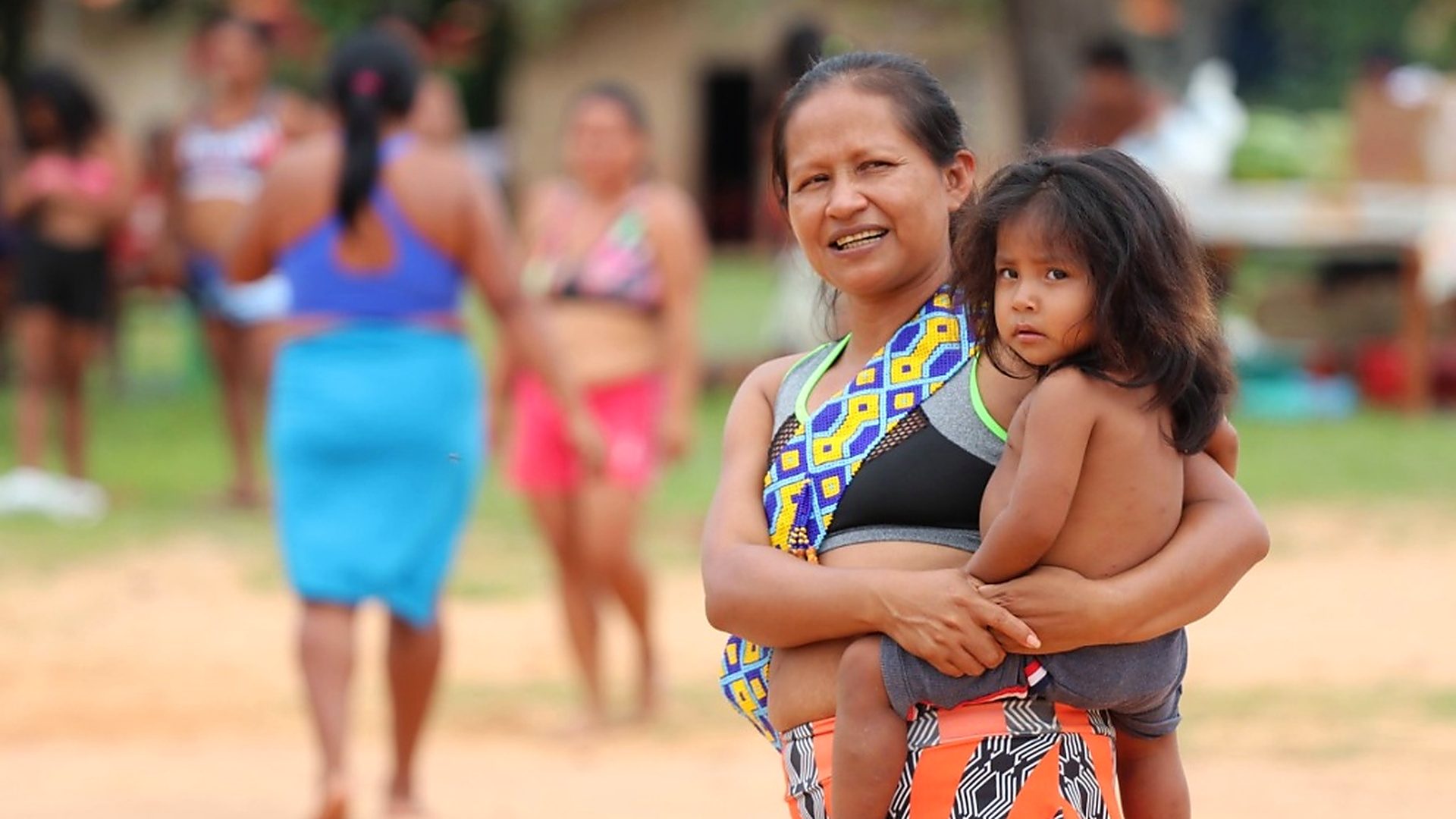 Mulher indígena segurando uma criança no colo durante encontro na aldeia